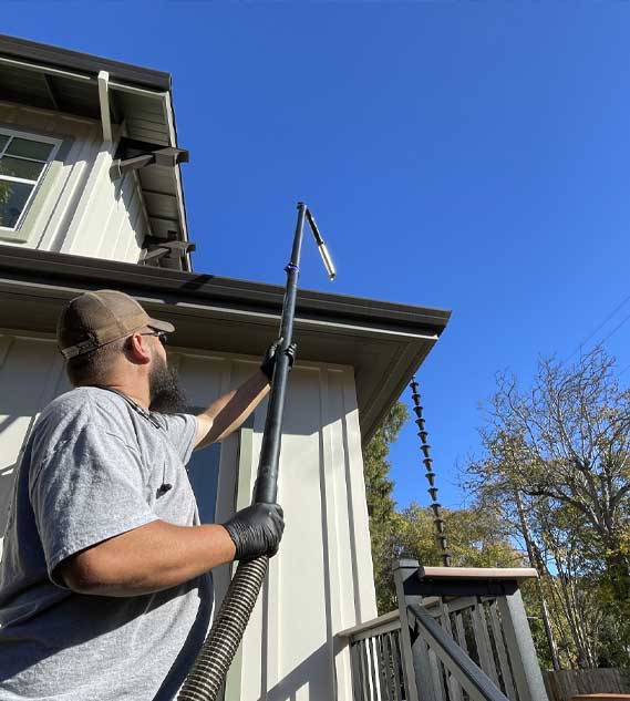 A person using the carbon clamping pole and carbon swan neck to clear the gutter of a house.