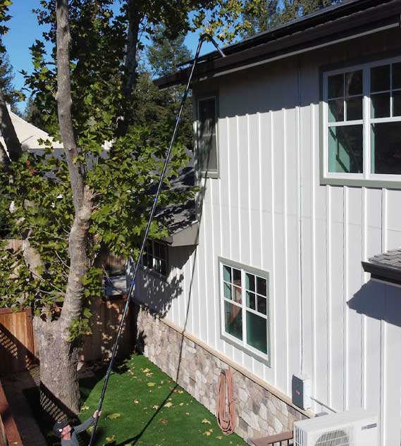 A person using a 20-foot carbon clamping pole and carbon swan neck to remove gutter debris from a house.