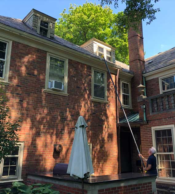 A homeowner performing gutter maintenance on their residence with the carbon push-fit pole and silicon U-bend neck.