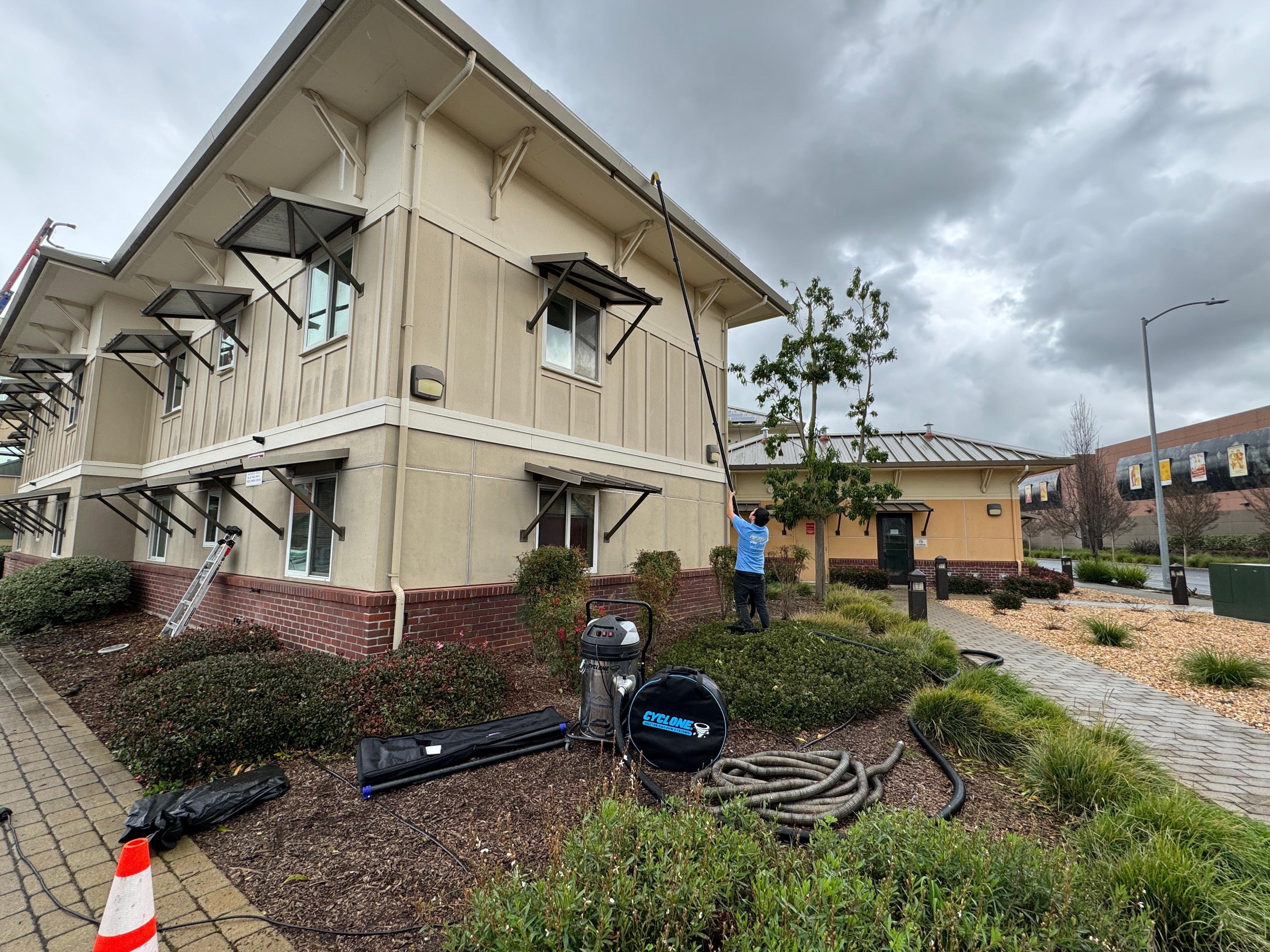 A man cleaning a gutter on a building using a gutter vacuum system.