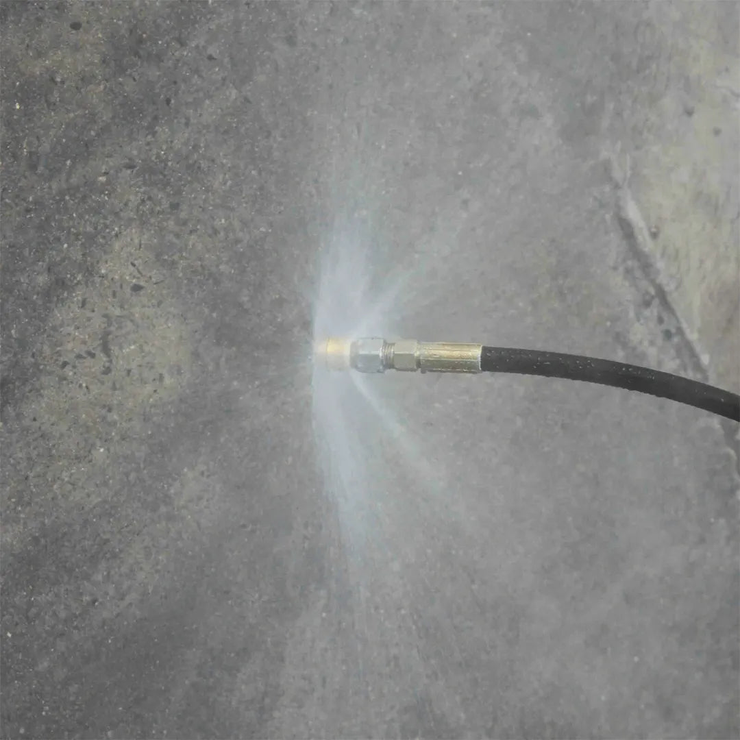 Spinning Jetting for Drain Line Cleaning - 1/4" NPT, 4000 PSI, 045 Orifice, attached to a black hose spraying a wide water fan across concrete